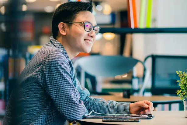 Lächelnde Person, die an einem Tisch sitzt und mit einer anderen Person (nicht sichtbar) spricht